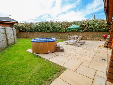 An outdoor patio with a hot tub lawn chairs table with umbrella and a barbecue at Ash Lodge in Greetham Rutland