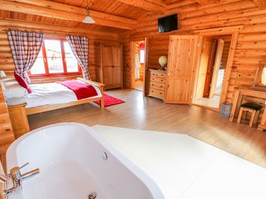 A bedroom with a large bed a bathtub wooden furniture and plaid curtains at Ash Lodge in Greetham Rutland
