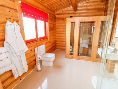 A bathroom with a toilet a wooden sauna a shower and white robes on hooks at Ash Lodge in Greetham Rutland