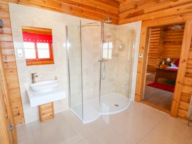 A bathroom with a glass shower enclosure and a white sink next to a wooden door leading to a bedroom at Ash Lodge in Greetham Rutland