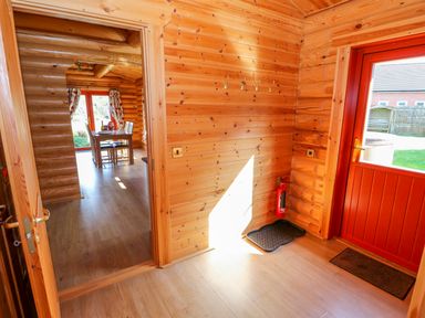 An interior view of a wooden cabin with a door leading to a dining area and a red door opening to a garden at Ash Lodge in Greetham Rutland