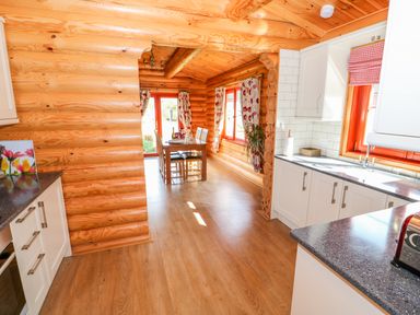A kitchen and dining area with wooden log walls and white cabinets at Ash Lodge in Greetham Rutland