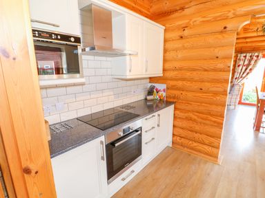 A kitchen with white cabinets black electric stove and oven wooden log walls at Ash Lodge in Greetham Rutland