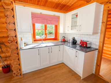 A kitchen with white cabinets a window with a red checkered blind and red appliances at Ash Lodge in Greetham Rutland