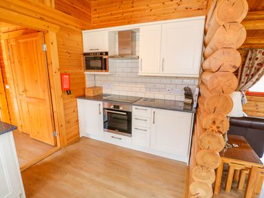 A kitchen with white cabinets a built in oven and microwave wooden walls and floor at Ash Lodge in Greetham Rutland