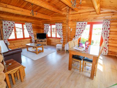 A living room and dining area with floral curtains wooden furniture and a television at Ash Lodge in Greetham Rutland