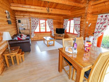 A living room with wooden furniture a dining table chairs a sofa a coffee table a television and floral curtains at Ash Lodge Greetham Rutland