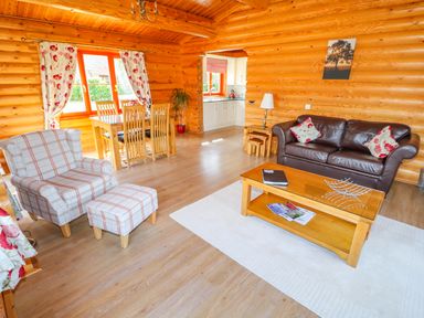 A living room with a brown leather sofa and plaid armchair next to a wooden dining table and kitchen at Ash Lodge Greetham Rutland