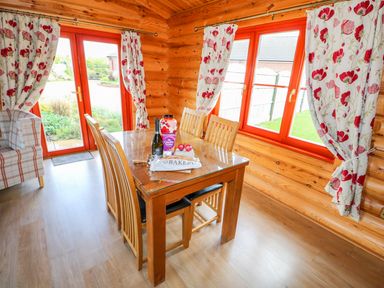 A dining area with a wooden table and chairs by windows with floral curtains at Ash Lodge Greetham Rutland