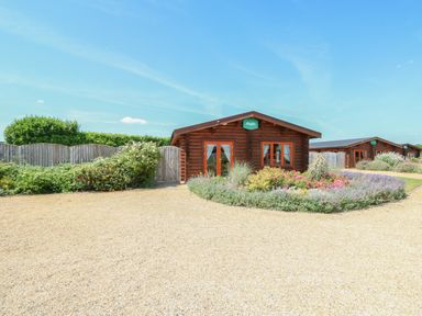 A gravel driveway with a flower bed in front of wooden lodges at Ash Lodge in Greetham Rutland