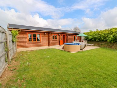 A wooden cabin with a patio a hot tub outdoor furniture and a green lawn at Yew Lodge in Greetham Rutland