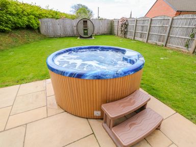 A backyard with a hot tub on a tiled patio and wooden fencing in the background at Yew Lodge in Greetham Rutland