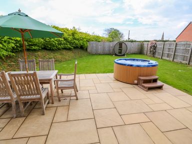 A garden patio with outdoor dining table umbrella wooden chairs hot tub and fenced lawn at Yew Lodge Greetham Rutland