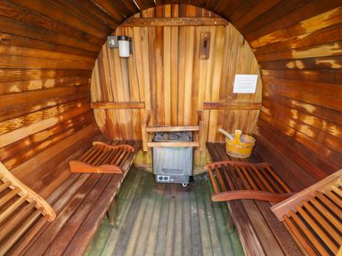 An interior view of a wooden barrel sauna with benches a heater a bucket and ladle at Yew Lodge in Greetham Rutland