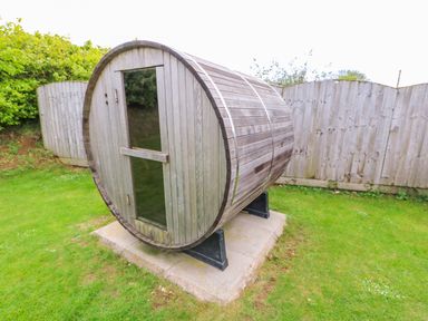 A wooden barrel-shaped outdoor sauna on a concrete base in a grassy backyard at Yew Lodge in Greetham Rutland