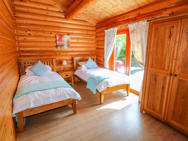 A bedroom with two single beds a wooden wardrobe and a door with curtains at Yew Lodge Greetham Rutland