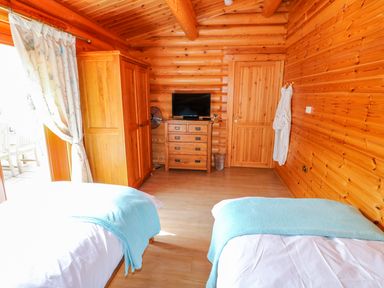 A bedroom with two beds a wooden wardrobe a chest of drawers with a TV and a wooden door at Yew Lodge in Greetham Rutland