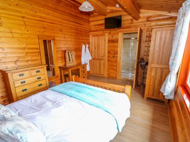 A bedroom with a wooden bed a dresser a vanity table a wardrobe and an open door showing a shower at Yew Lodge Greetham Rutland