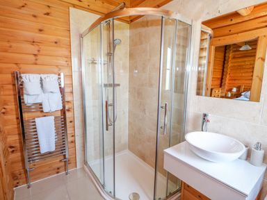A bathroom with a corner glass shower enclosure a white sink on a wooden vanity and a towel rack with towels at Yew Lodge in Greetham Rutland