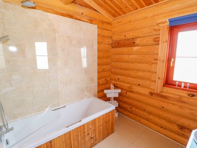 A bathroom with a bathtub wooden walls a window and a towel rack at Yew Lodge Greetham Rutland