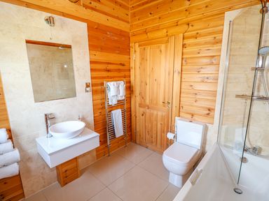 A bathroom with a white sink and mirror beside a toilet and bathtub with shower at Yew Lodge Greetham Rutland