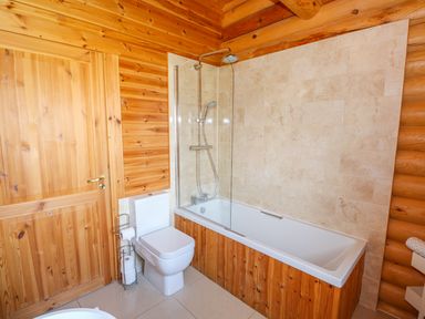 A bathroom with a bathtub with shower next to a toilet and wooden walls at Yew Lodge in Greetham Rutland