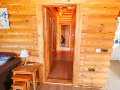 A wooden hallway viewed through a door opening with a side table and lamp beside a brown leather couch at Yew Lodge in Greetham Rutland