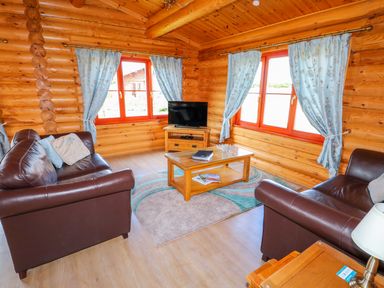 A living room with brown leather sofas a wooden coffee table a TV on a wooden stand and windows with blue curtains at Yew Lodge in Greetham Rutland
