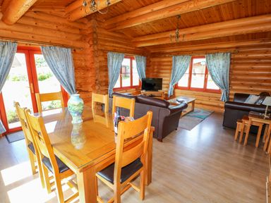 A log cabin living and dining area with wooden furniture leather sofas a television and blue curtains at Yew Lodge in Greetham Rutland
