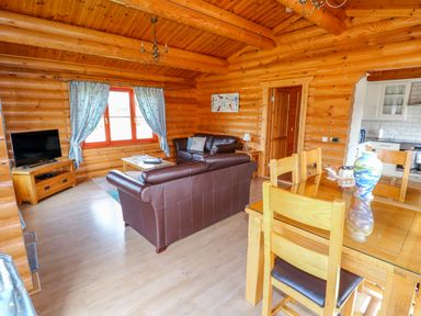 A living room with brown leather sofas a wooden dining table with chairs a TV on a stand and kitchen view at Yew Lodge Greetham Rutland