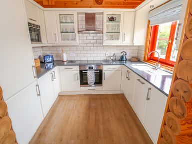 A kitchen with white cabinets a stainless steel oven a blue toaster a kettle glass shelves and a window with a blind at Yew Lodge Greetham Rutland