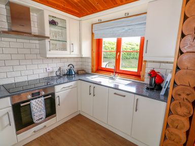 A kitchen with white cabinets a window with blue checkered blind a kettle and a coffee machine at Yew Lodge in Greetham Rutland