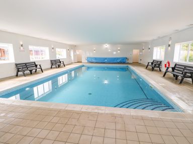An indoor swimming pool with benches along the walls at Yew Lodge in Greetham Rutland