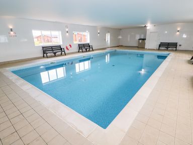 An indoor swimming pool with benches along the walls and windows showing wooden buildings outside at Yew Lodge in Greetham Rutland
