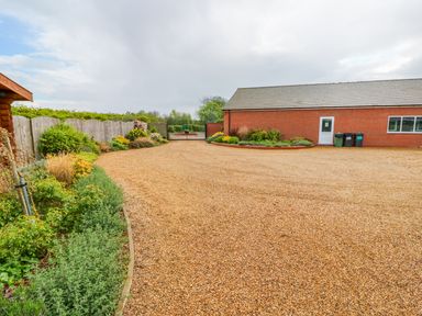 A gravel driveway with garden beds and a brick building with bins at Yew Lodge in Greetham Rutland