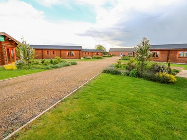 A pathway with grass and shrubs leading to wooden cabin buildings at Yew Lodge in Greetham Rutland