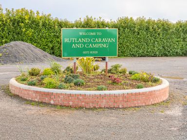 A round flower bed with a welcome sign for Rutland Caravan and Camping in an outdoor area with gravel and hedges