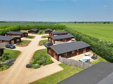 An aerial view of multiple wooden lodges with patios and parked cars surrounded by green fields at Yew Lodge in Greetham Rutland