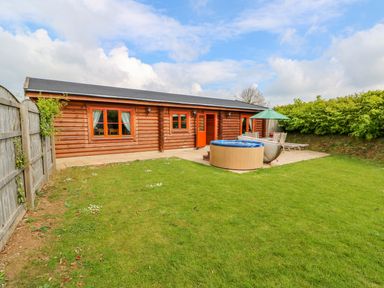 A garden with a patio hot tub wooden deck chairs and a wooden house at Willow Lodge in Greetham Rutland