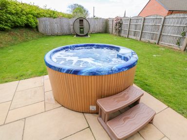 A backyard with a round hot tub with steps on a paved patio and a wooden fence with a circular sauna at Willow Lodge in Greetham Rutland