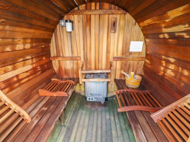 An interior of a wooden barrel sauna with benches a heater and wooden bucket with ladle at Willow Lodge in Greetham Rutland