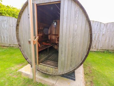 A wooden barrel sauna with an open door on a concrete base in a garden at Willow Lodge in Greetham Rutland