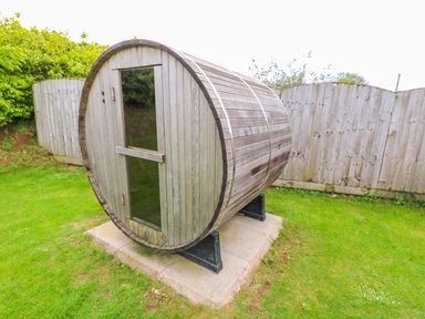 A wooden barrel sauna in a backyard with grass and a wooden fence at Willow Lodge in Greetham Rutland
