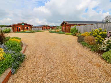 A gravel driveway with four wooden cabins and flower beds at Willow Lodge in Greetham Rutland