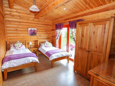 A bedroom with two single beds a wooden wardrobe and glass door with curtains at Willow Lodge in Greetham Rutland