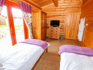 A bedroom with two single beds and purple blankets with a TV on a wooden chest of drawers and wooden wardrobe at Willow Lodge in Greetham Rutland