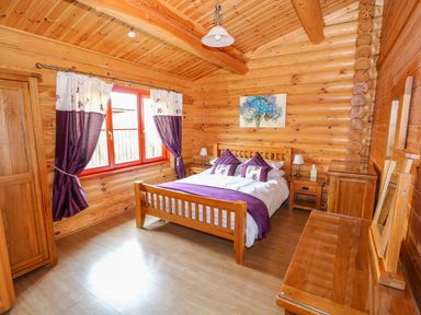 A bedroom with a wooden bed purple pillows and curtains wooden furniture and a window at Willow Lodge in Greetham Rutland