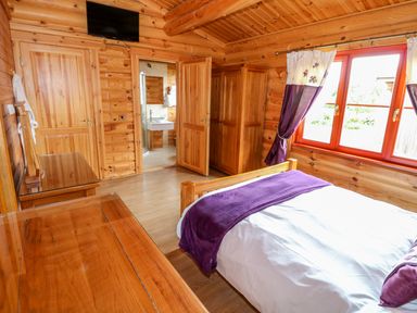 A wooden bedroom with a bed with purple blanket and pillow a wardrobe wooden furniture and a window at Willow Lodge in Greetham Rutland