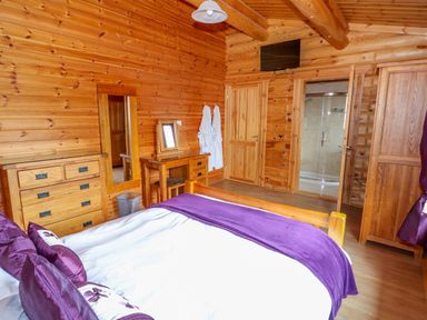 A bedroom with a wooden bed purple pillows and blanket wooden dresser dressing table mirror and open bathroom door at Willow Lodge in Greetham Rutland