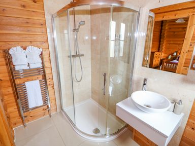 A bathroom with a corner glass shower enclosure a white sink on a countertop and folded towels on a heated rack at Willow Lodge in Greetham Rutland